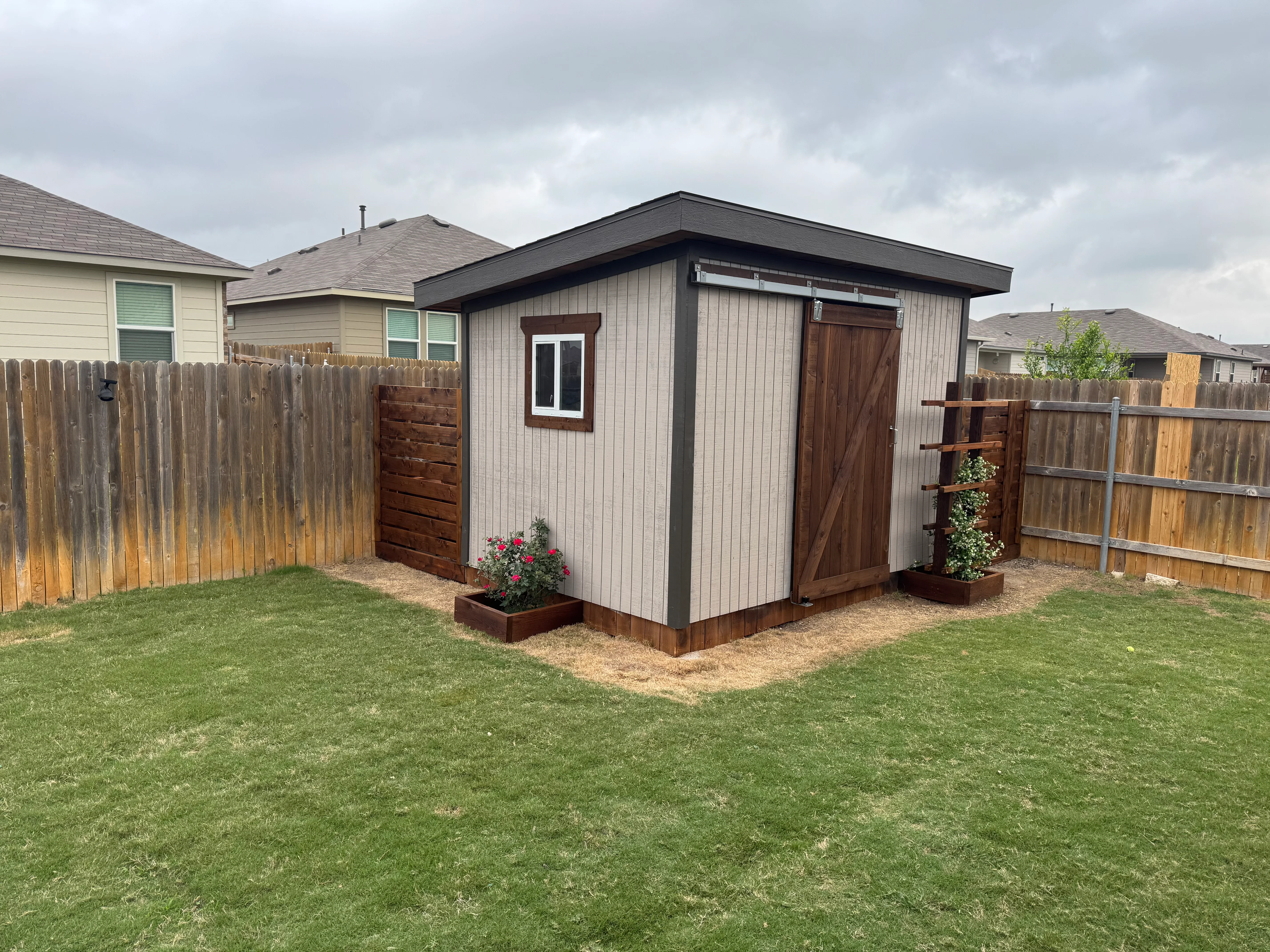Metal-sided shed with dark roof, wooden doors, and matching fence installation in residential backyard