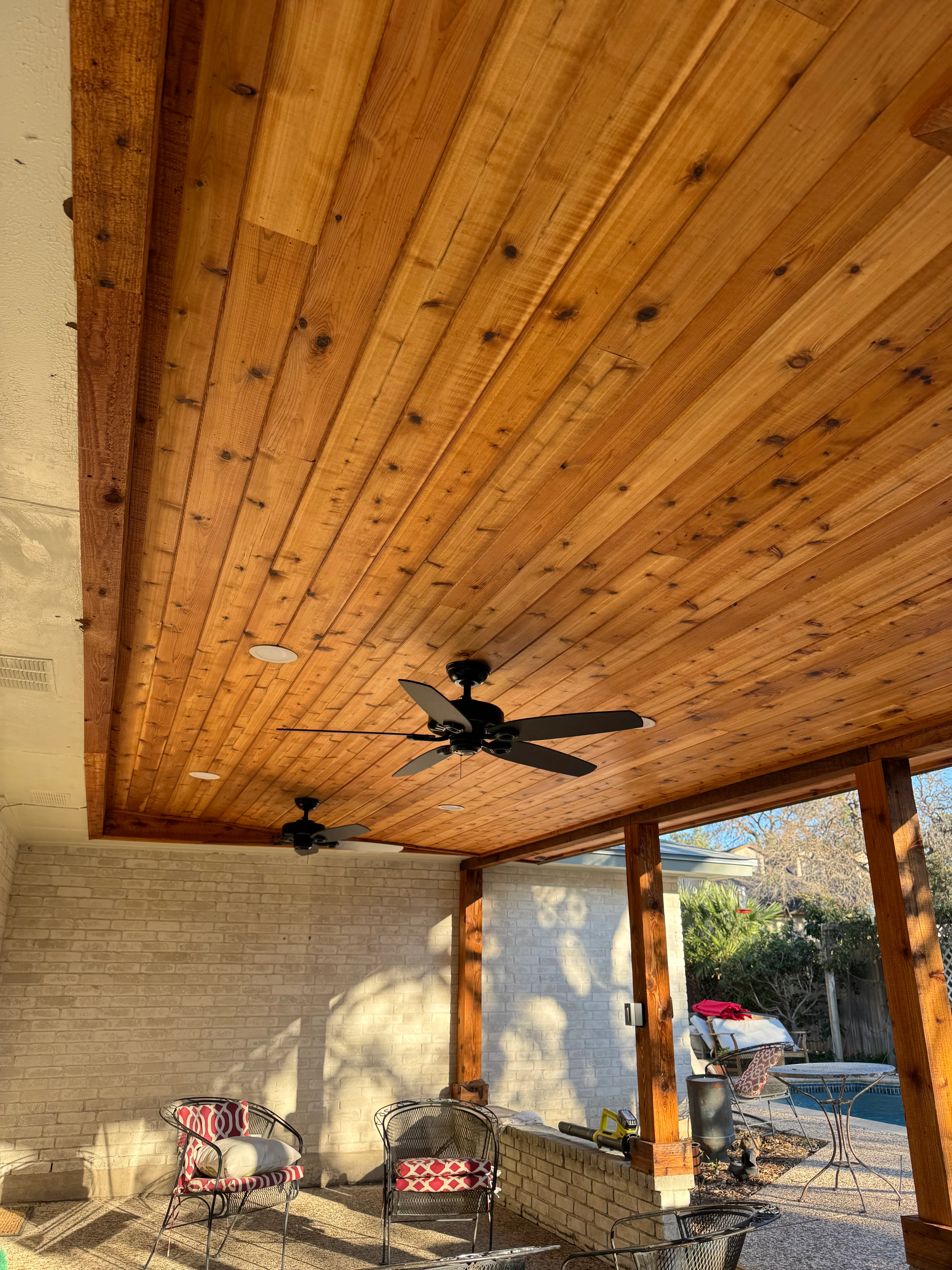 Wooden tongue-and-groove patio ceiling with timber beams, recessed lights, and ceiling fans