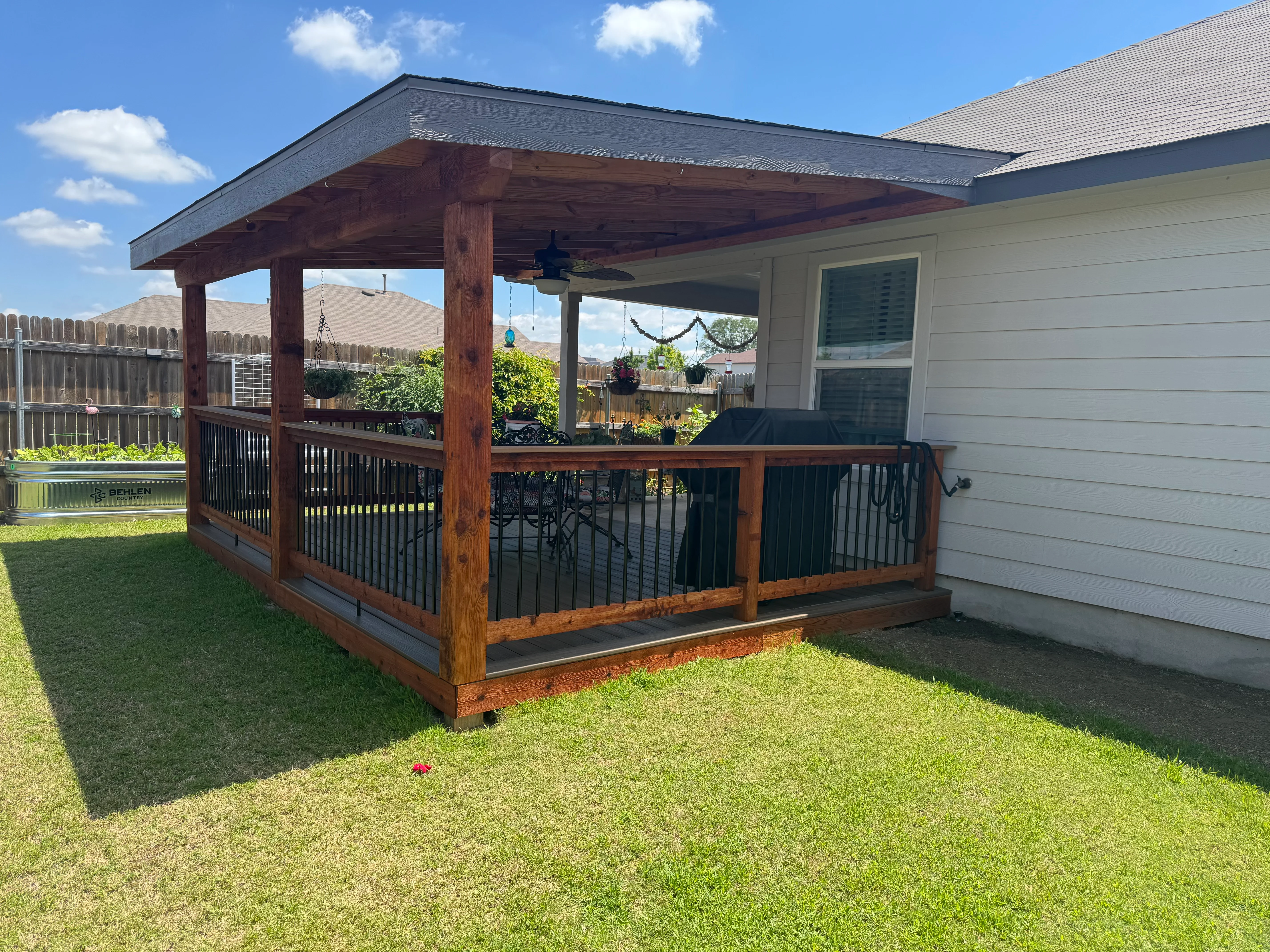 Covered deck with wood posts, metal roof, and black metal railings attached to house