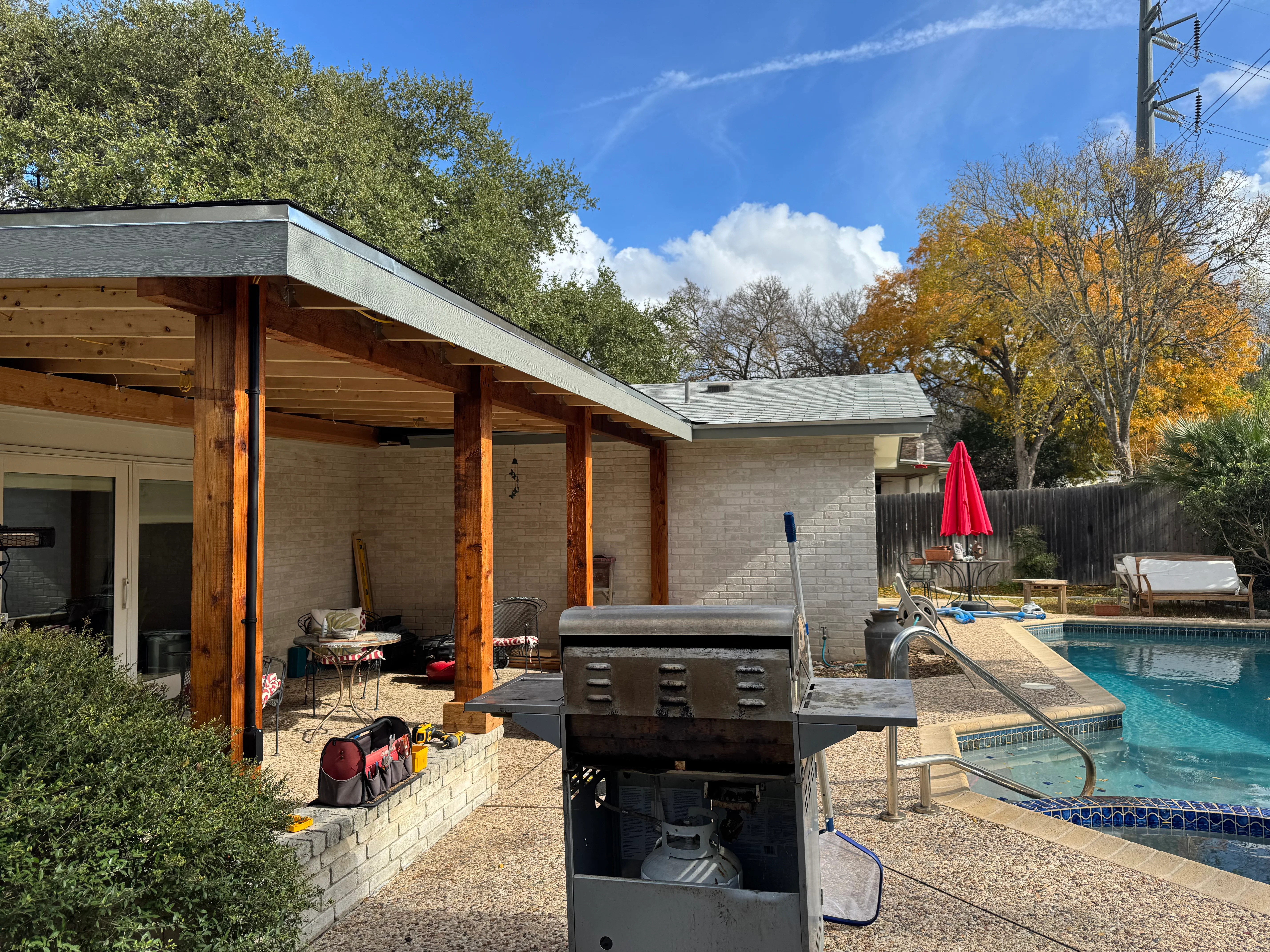 Cedar post patio shelter with metal roof overhang overlooking swimming pool