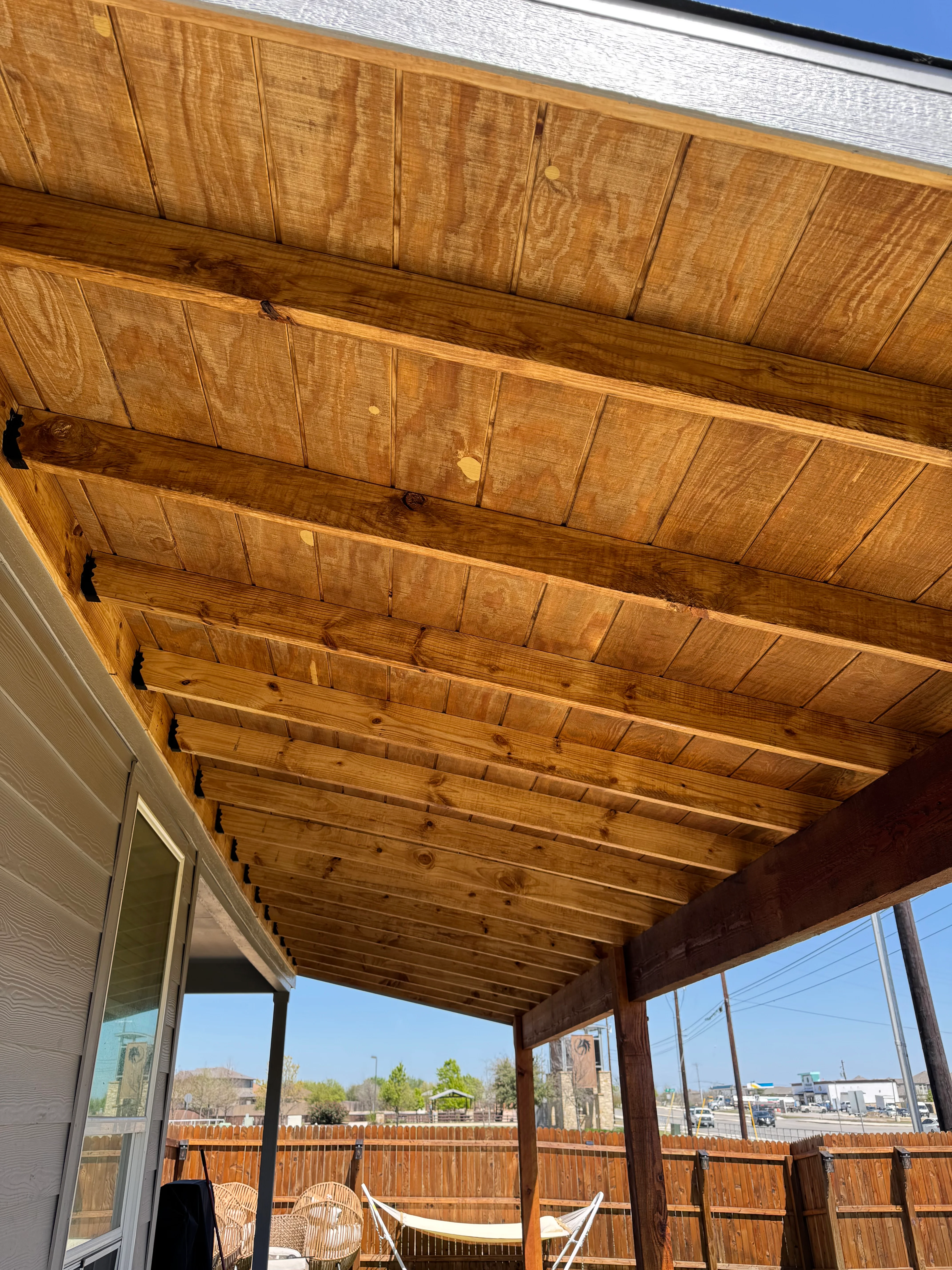 Wooden patio cover with exposed beams and tongue-and-groove ceiling panels, stained honey finish