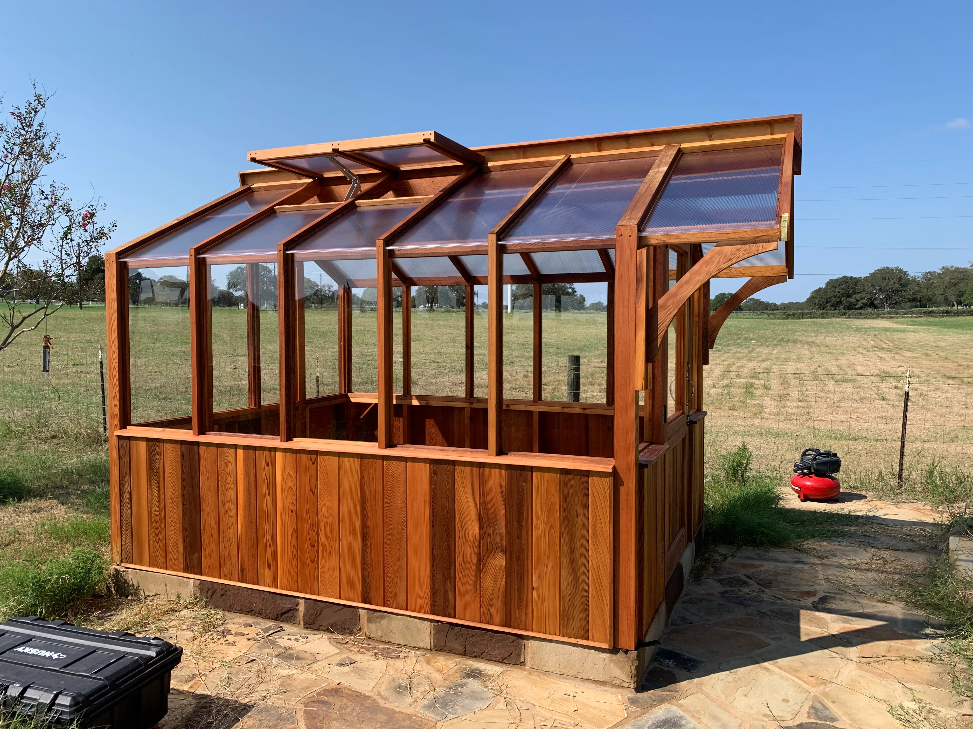 Cedar wood greenhouse with polycarbonate panels, solid wood base, and angled roof vents