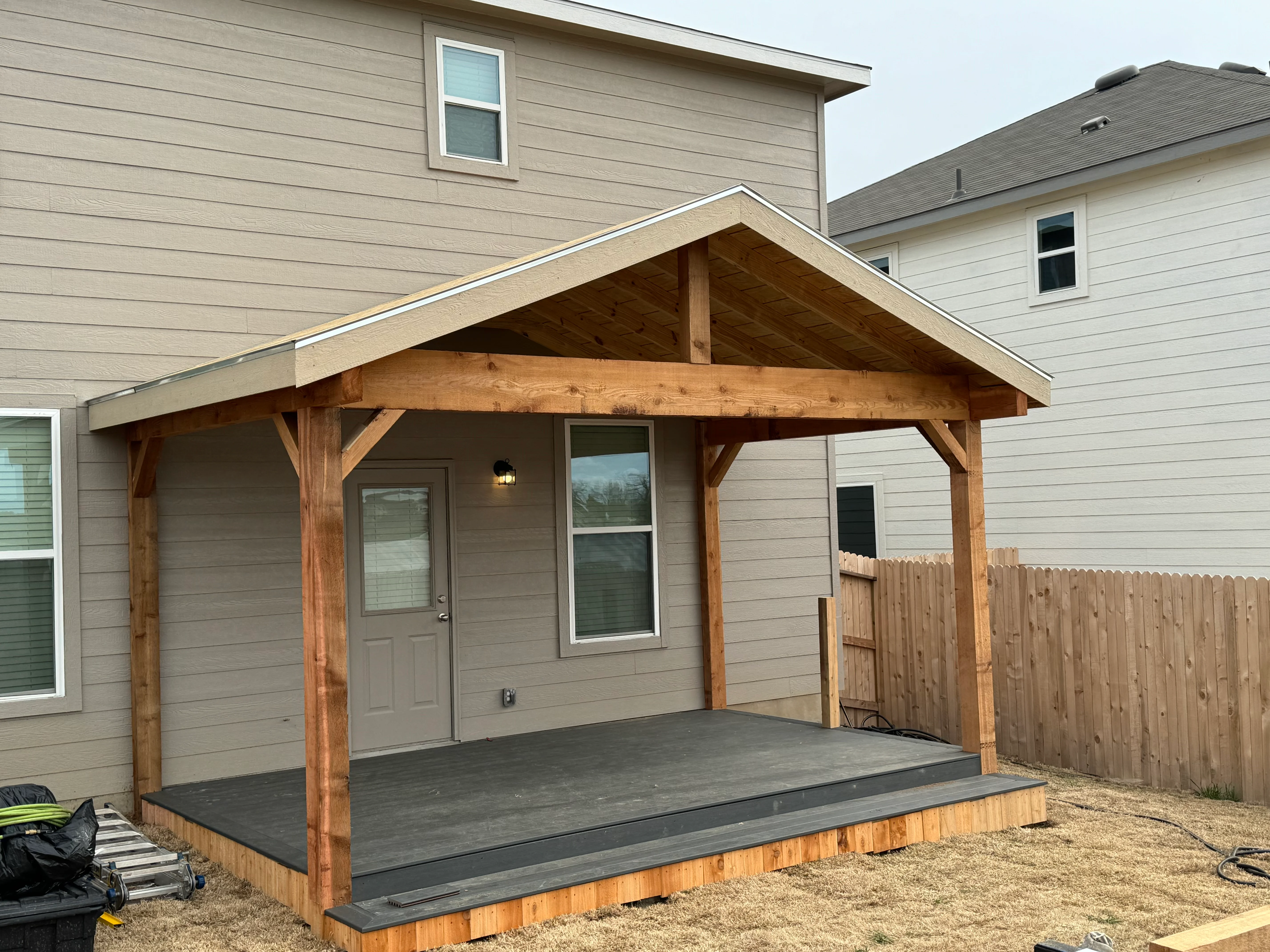 Timber frame covered patio with gable roof, exposed beams, and composite deck attached to residential home