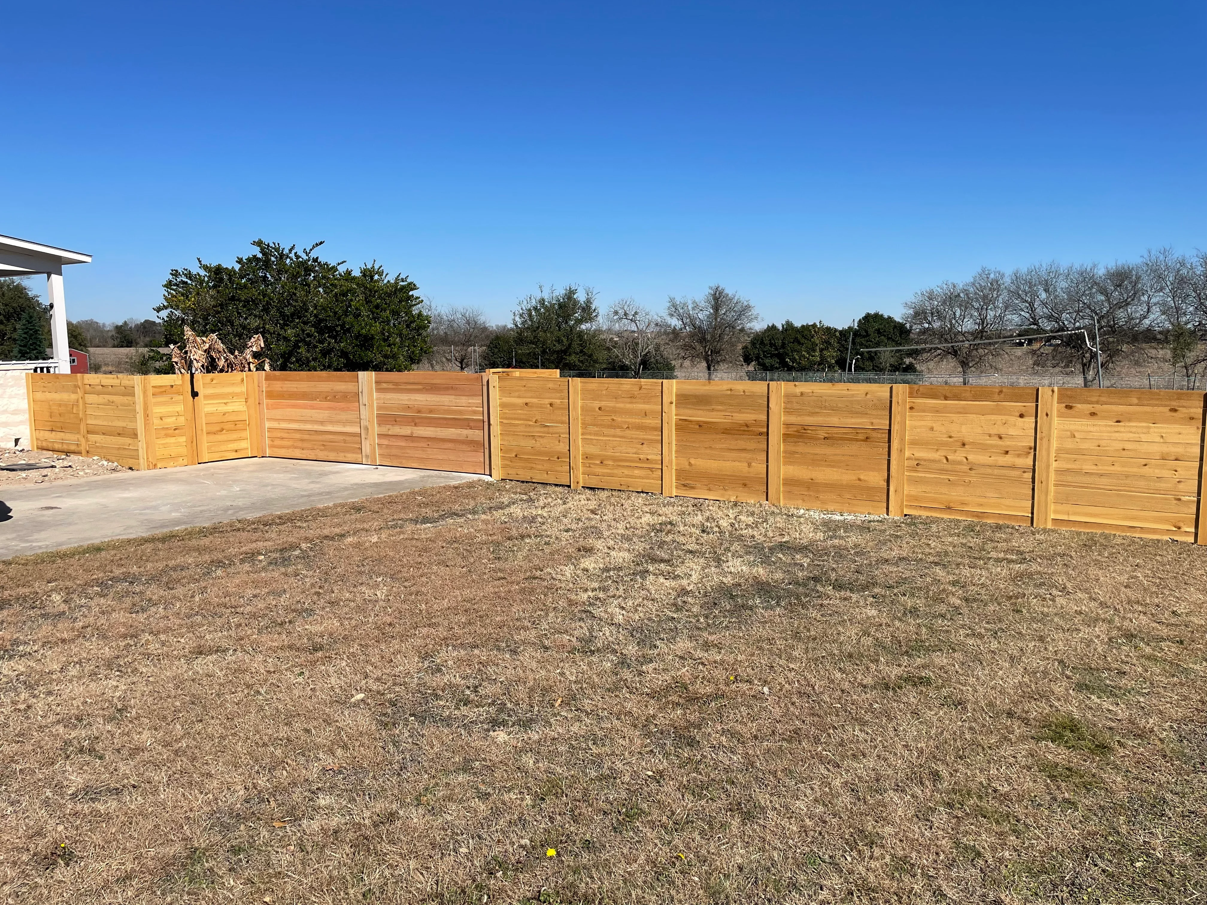 Horizontal cedar privacy fence with white posts installed along residential property perimeter