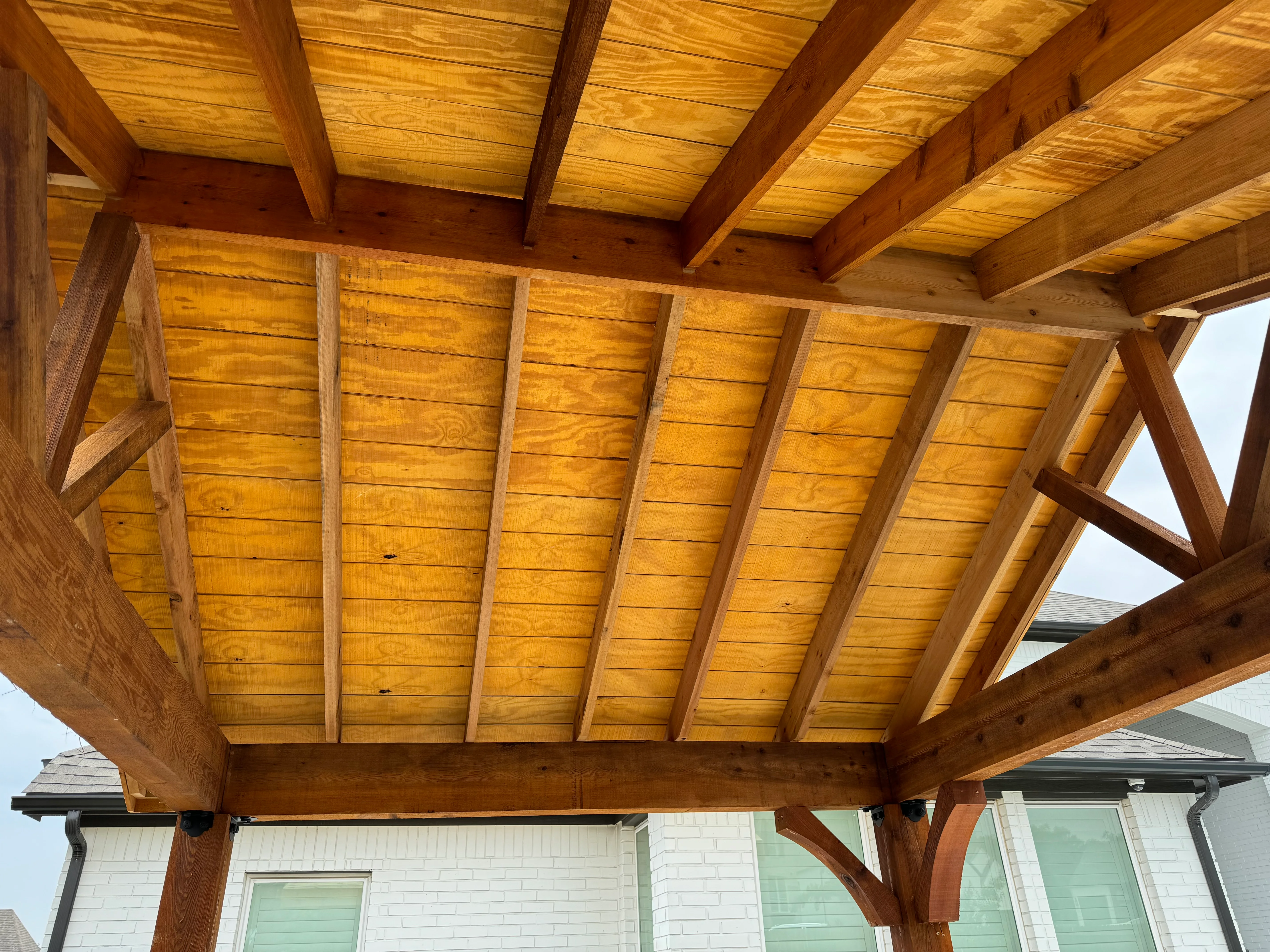 Stained wood pergola with beam construction and horizontal slat roof panels over patio