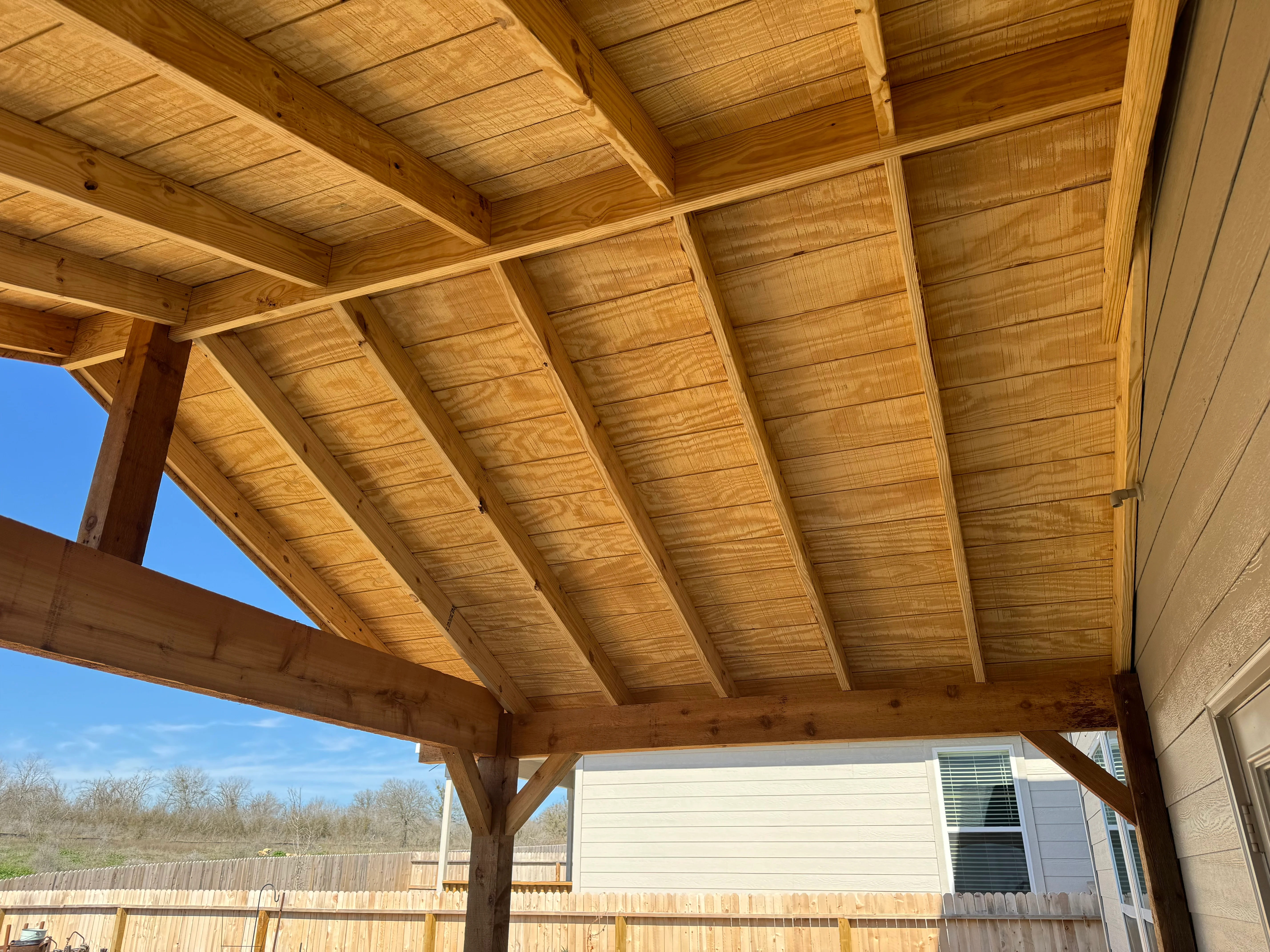 Timber frame patio cover with exposed beams and tongue-and-groove ceiling over composite deck