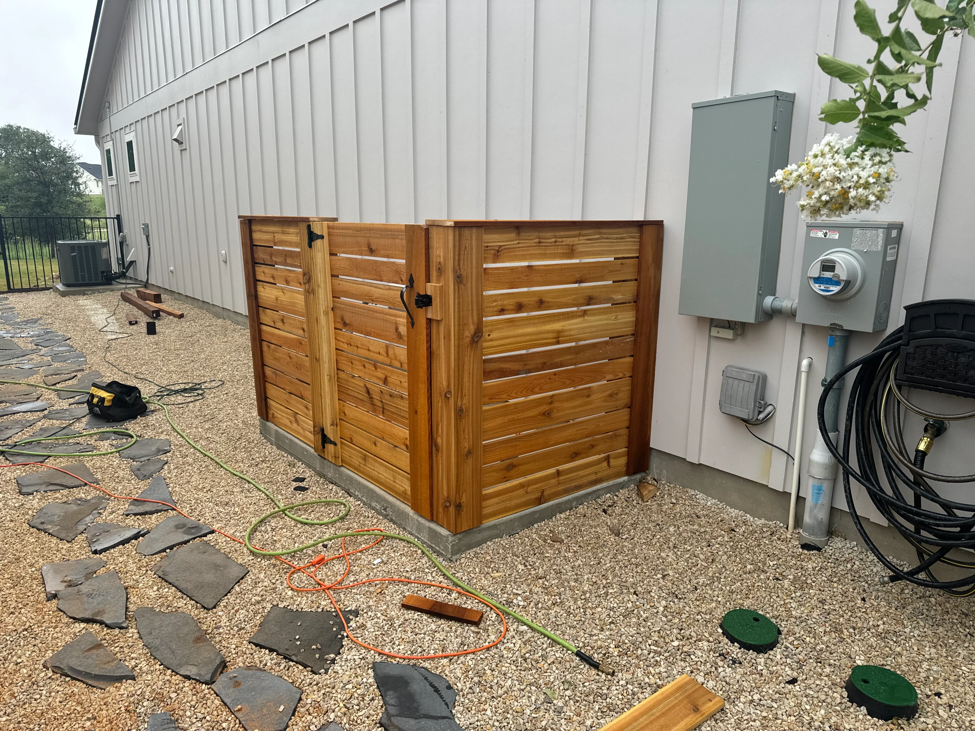 Cedar wood utility enclosure with horizontal slats and hinged doors on gravel patio