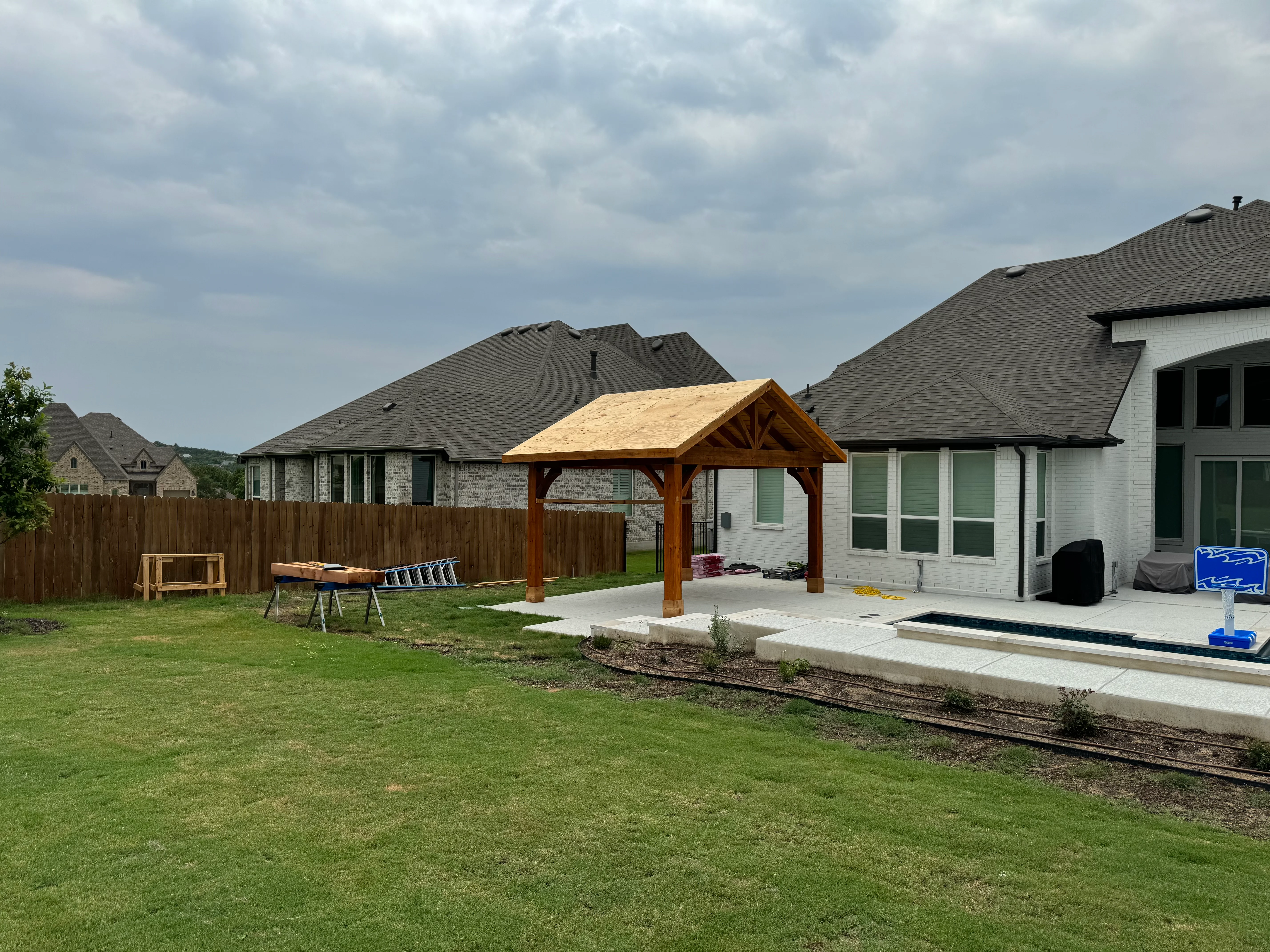 Timber frame pavilion with gable roof and concrete patio pad in residential backyard
