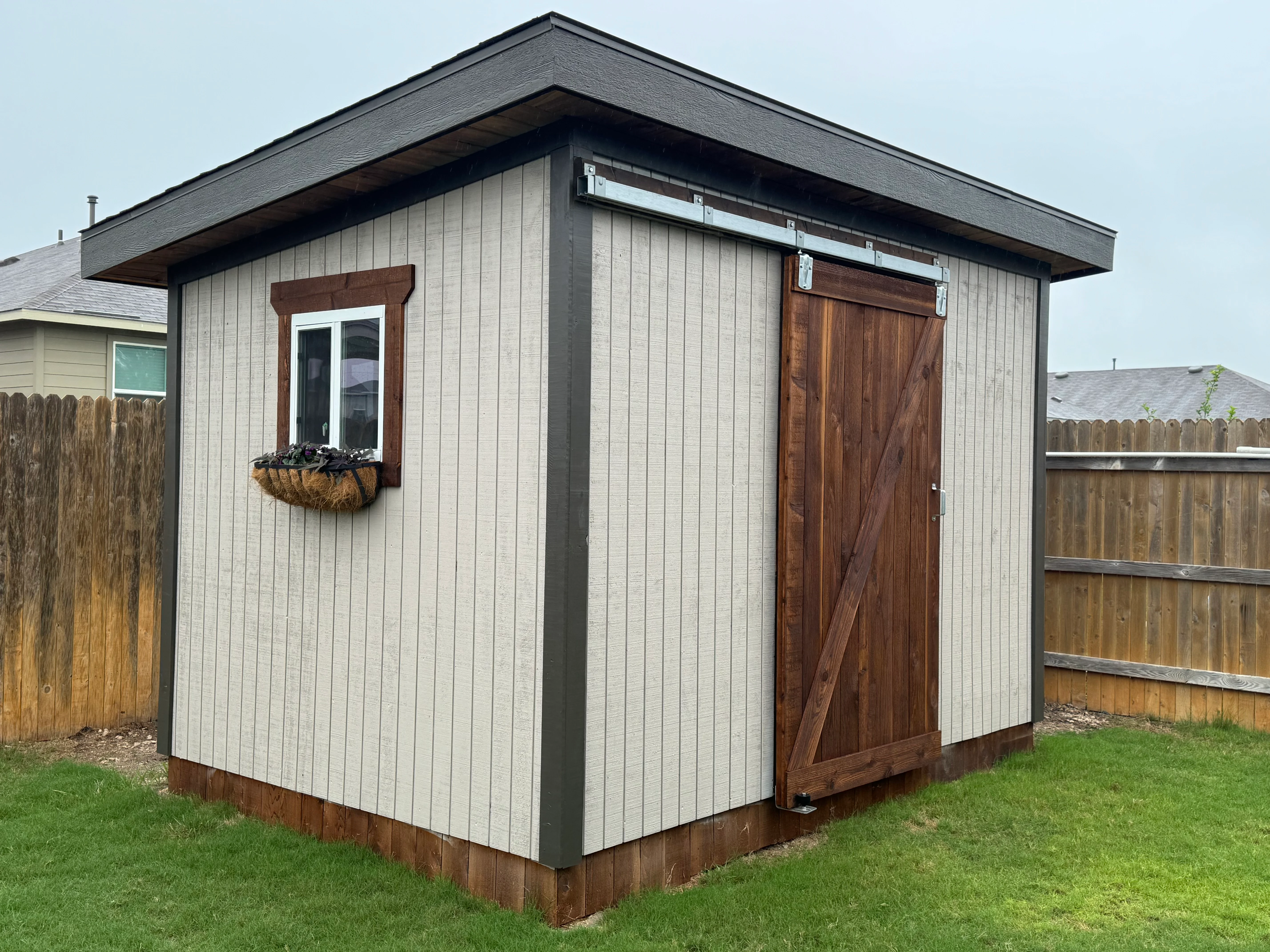 Modern garden shed with vertical siding, sliding barn door, and window with planter box