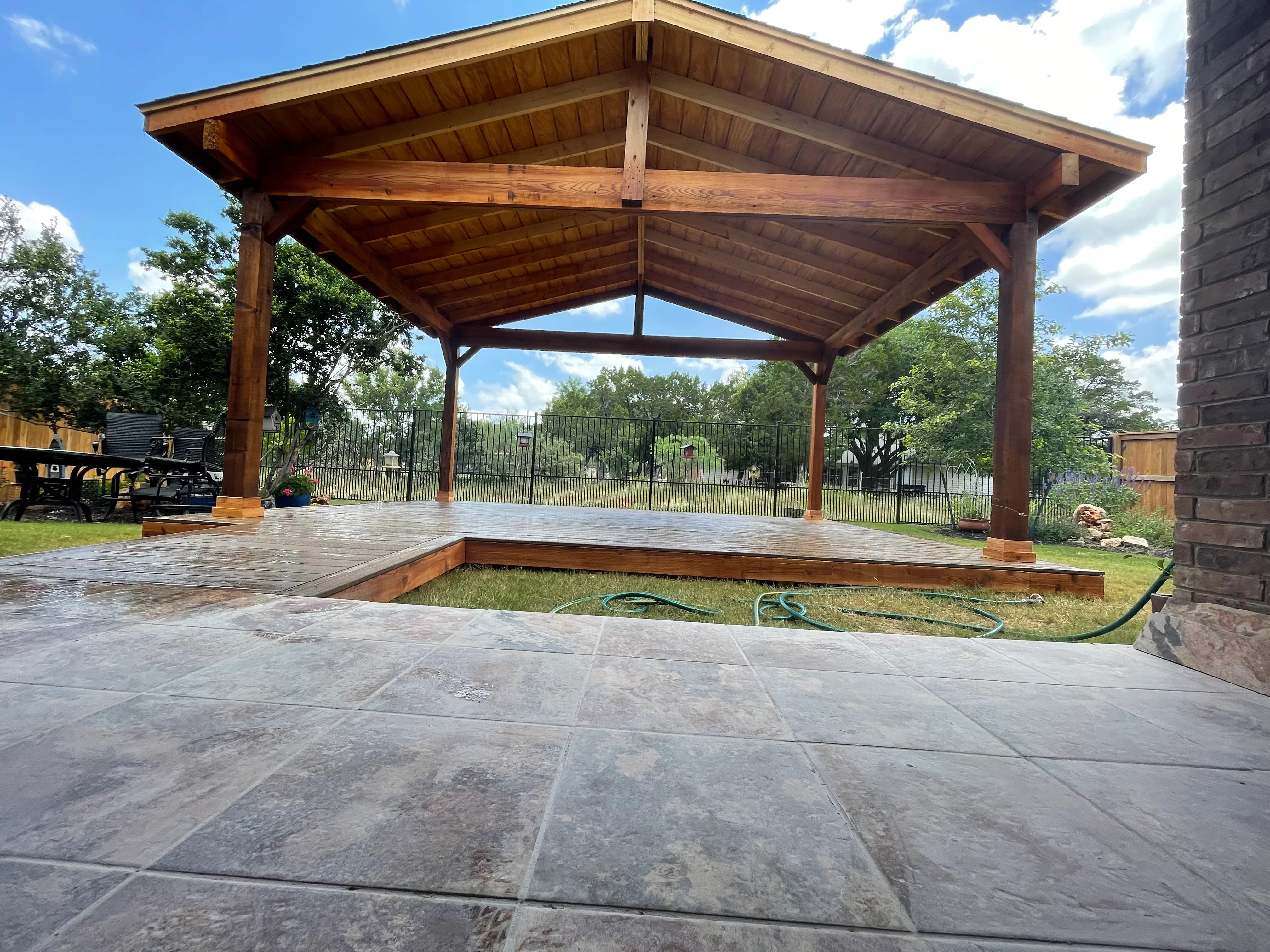 Timber pavilion with gable roof and composite deck platform over stamped concrete patio