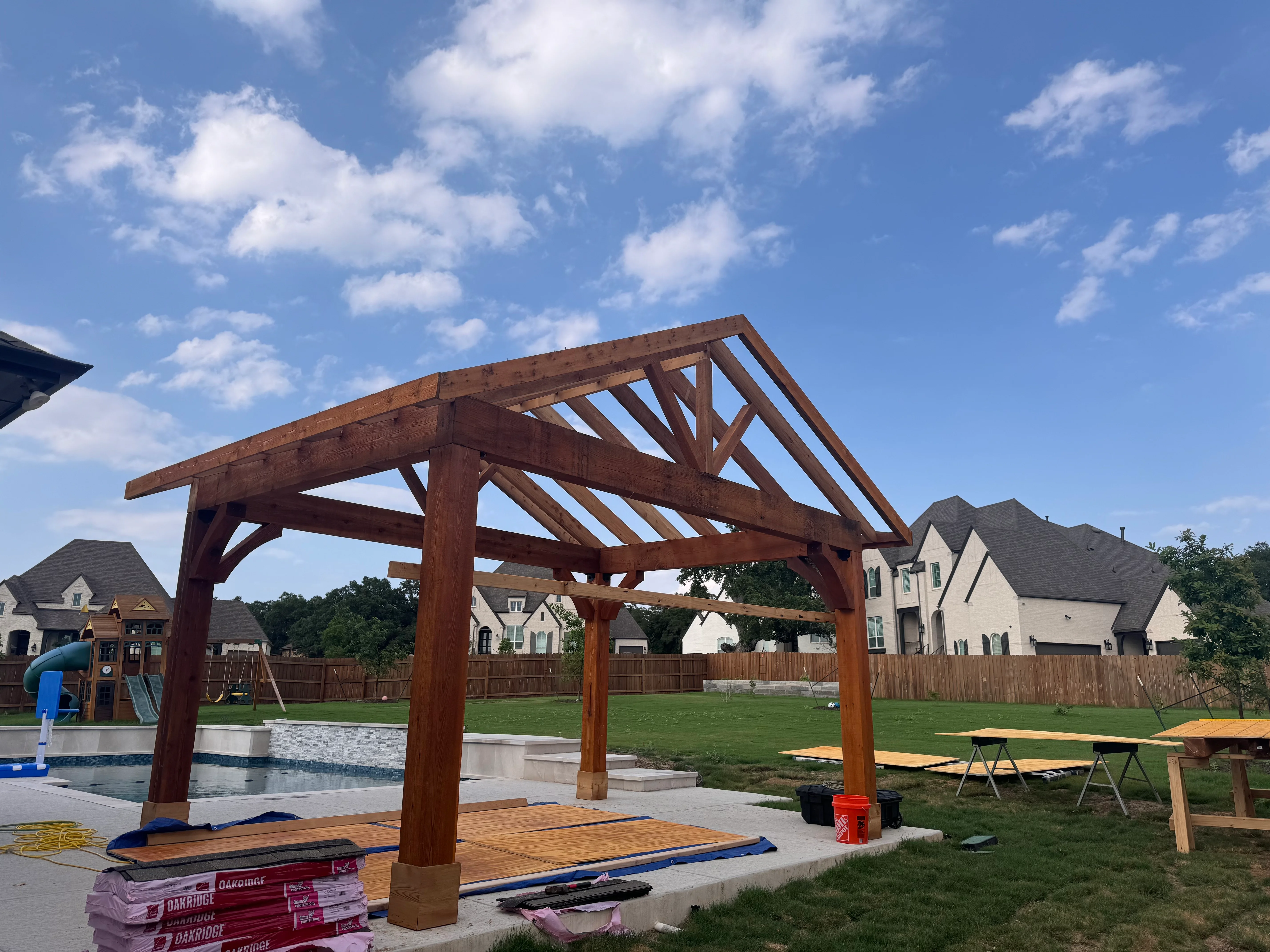 Timber frame pergola with exposed beams over composite pool deck in residential backyard