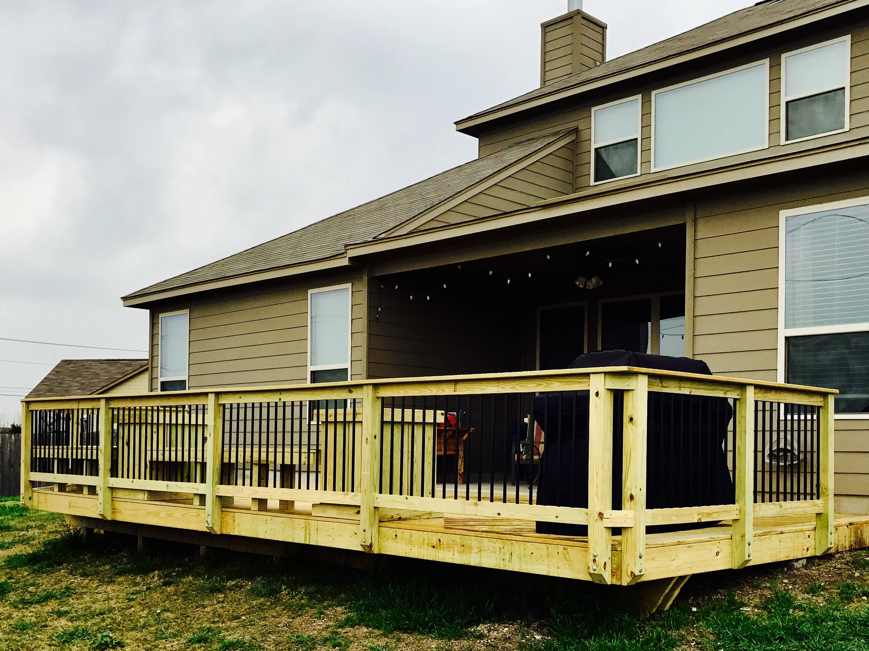 Pressure-treated wood deck with black aluminum spindle railing and posts attached to house