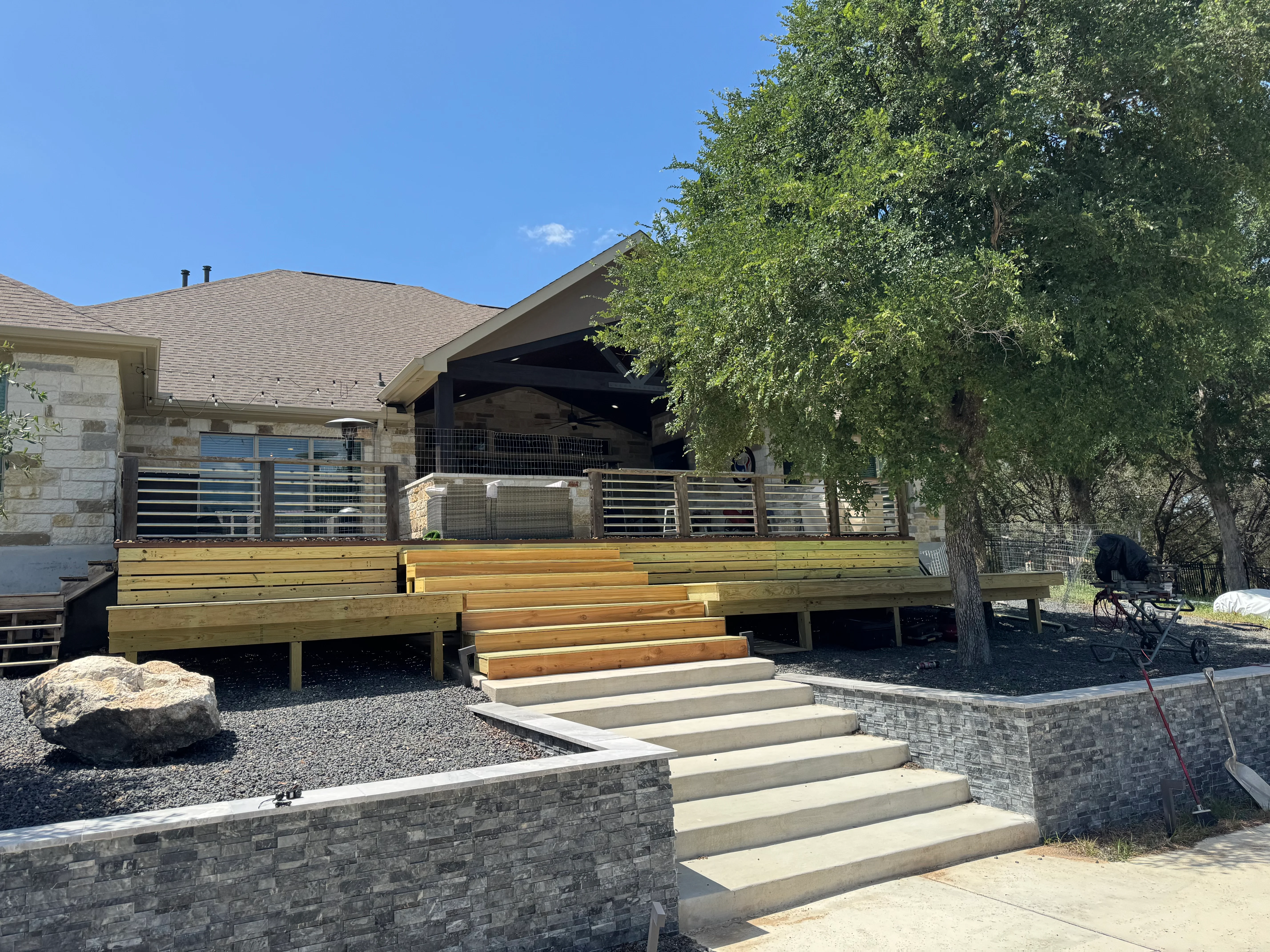 Elevated wood deck with metal horizontal railing, composite decking, and concrete paver steps with stone retaining walls