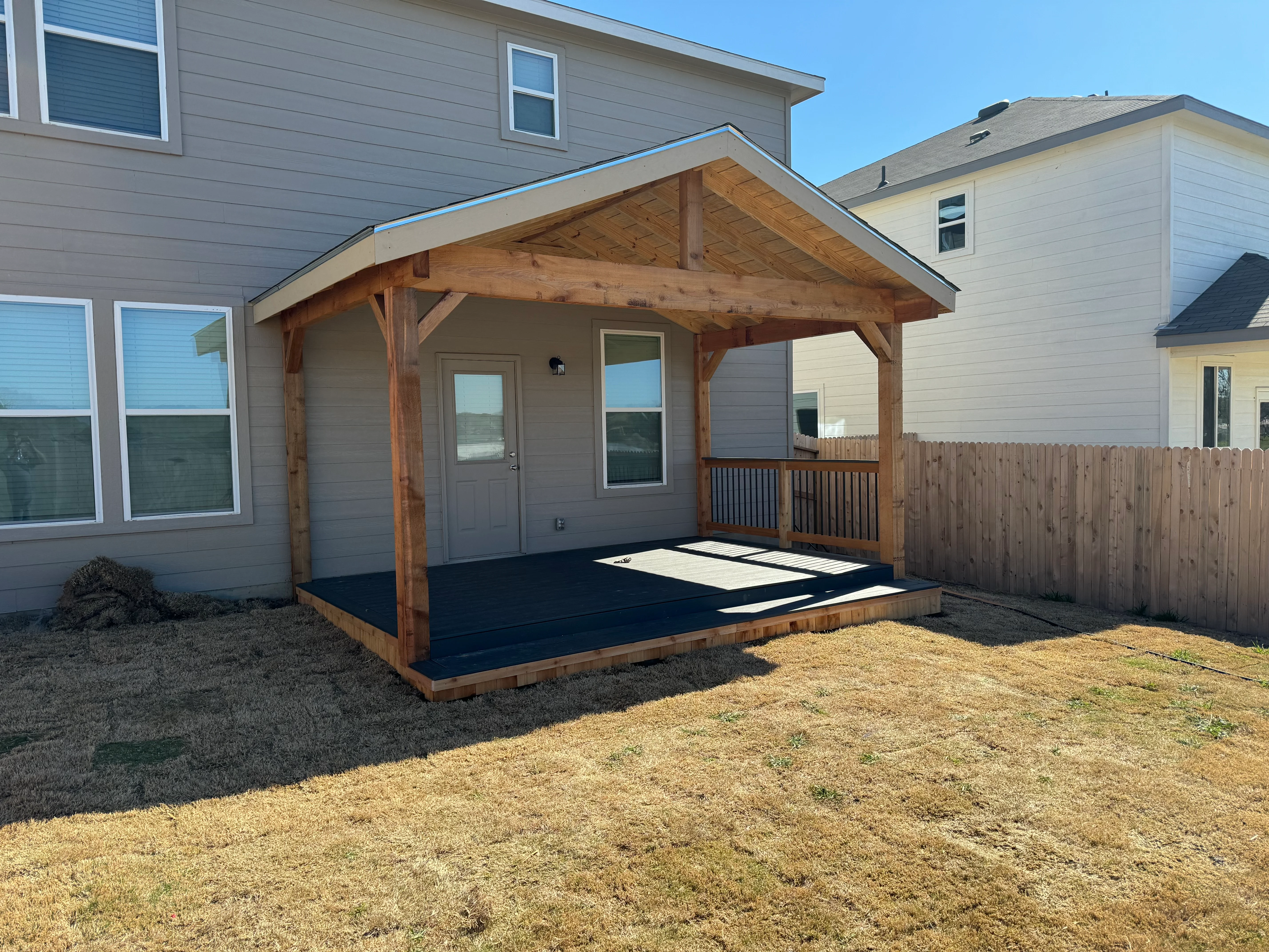 Timber frame covered patio with gabled roof, exposed beams, composite deck, and wooden railings attached to home