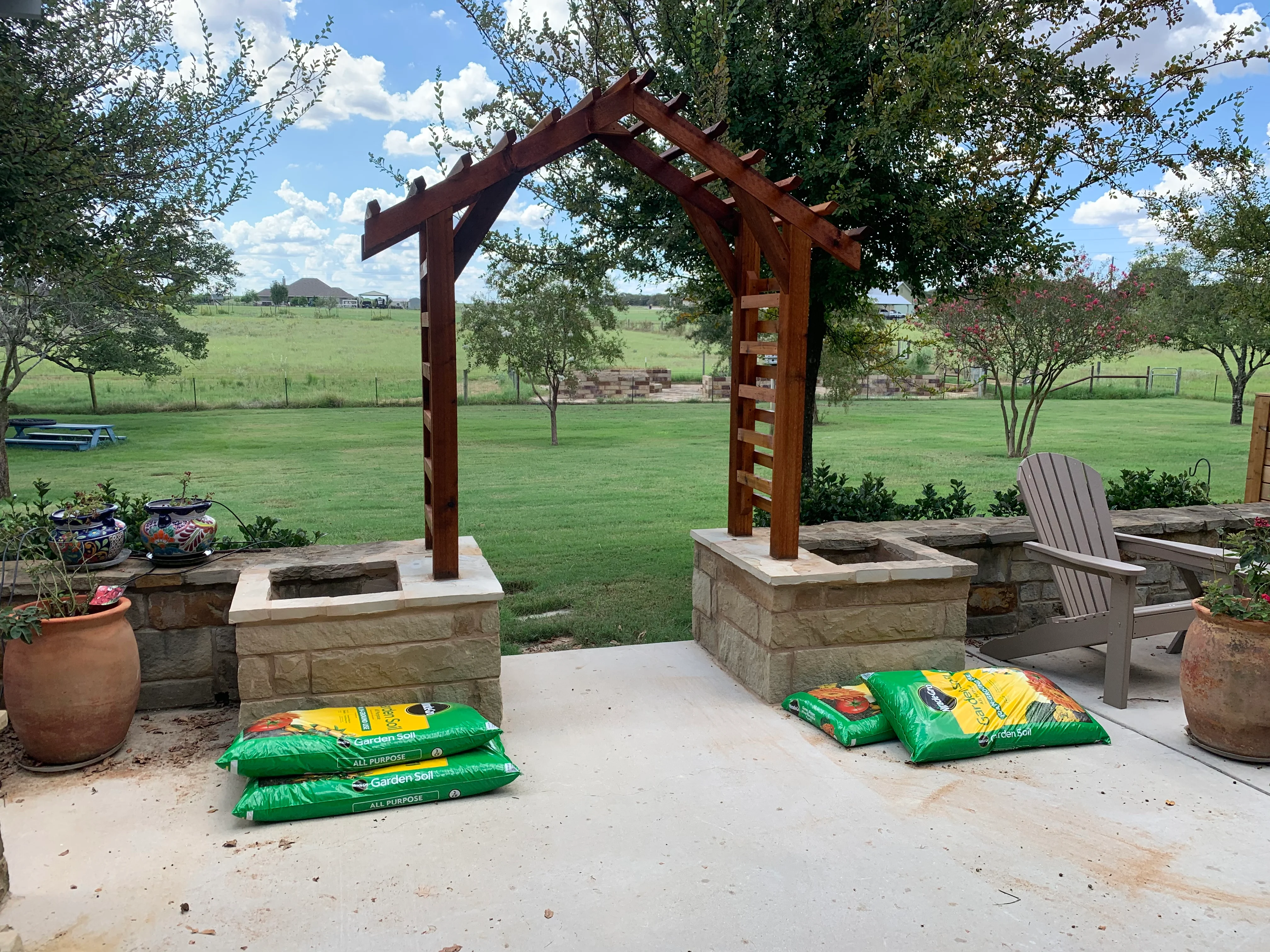 Stained wood pergola over stone fire pits with concrete patio and landscape plantings