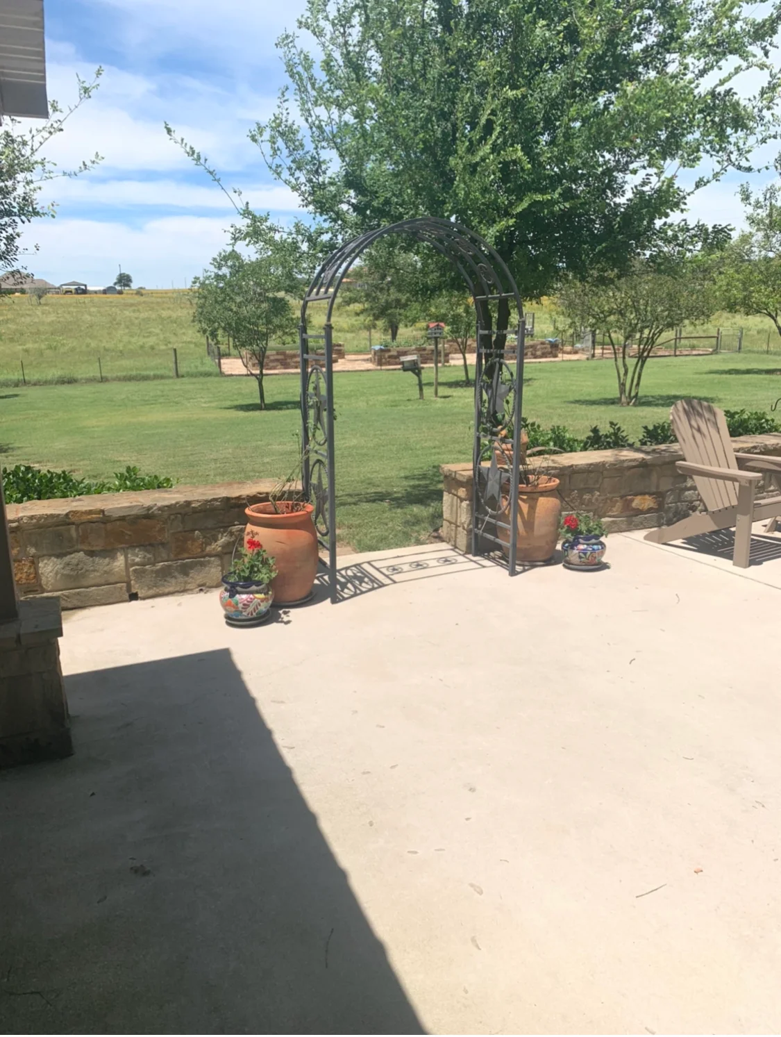 Concrete patio with stone retaining walls, black metal arbor, and Adirondack seating