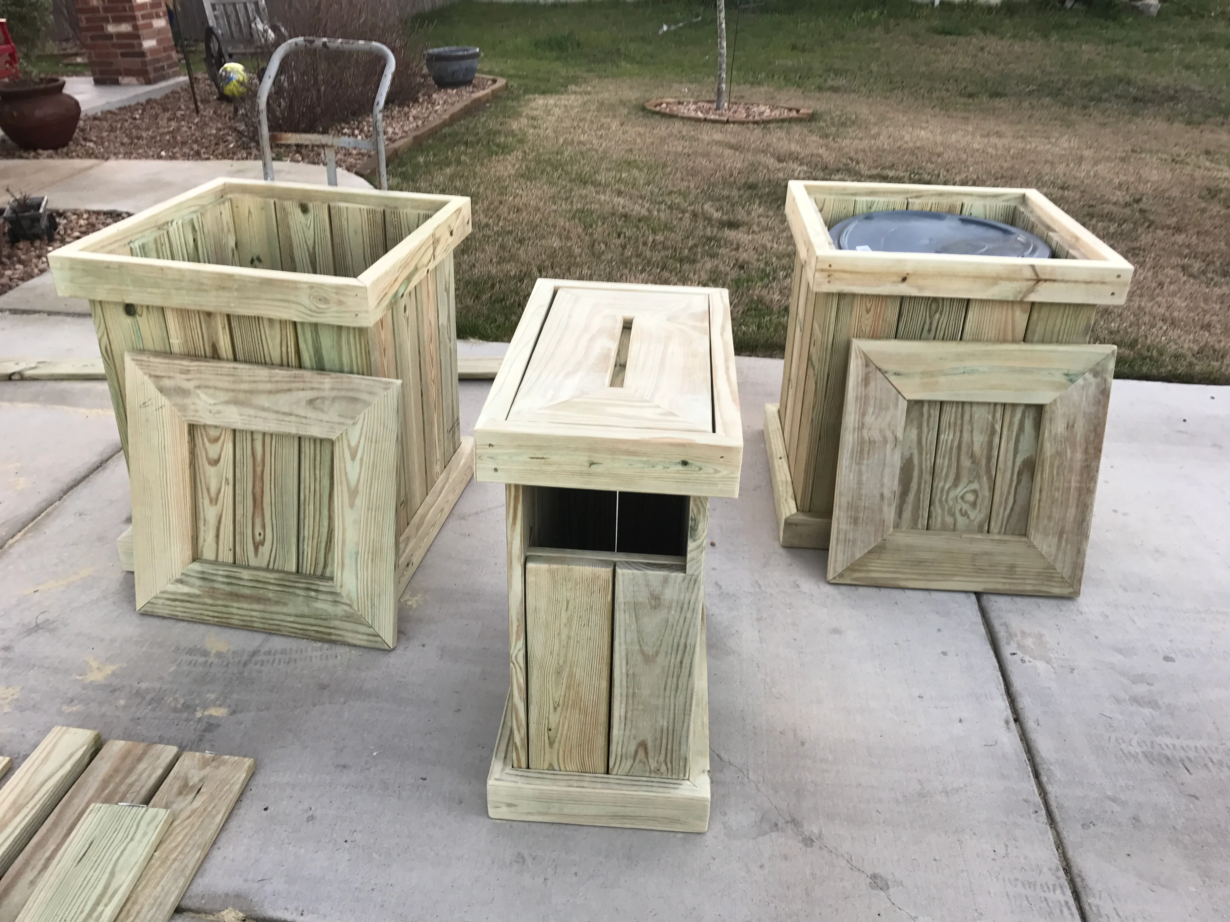 Three pressure-treated wood planters and pedestal with routed frames on concrete patio