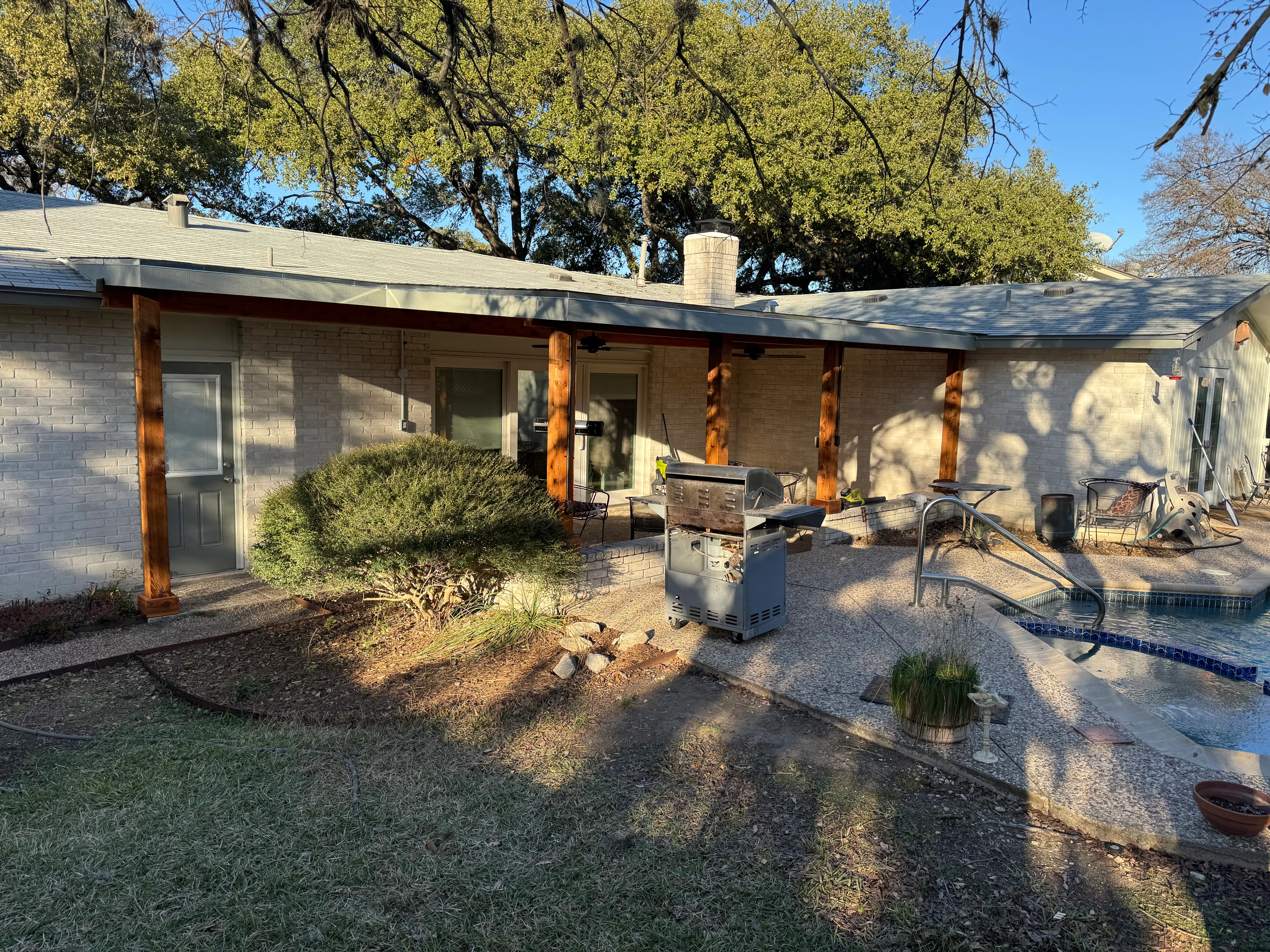 Covered patio with wooden posts, brick home, gravel surface, and outdoor kitchen