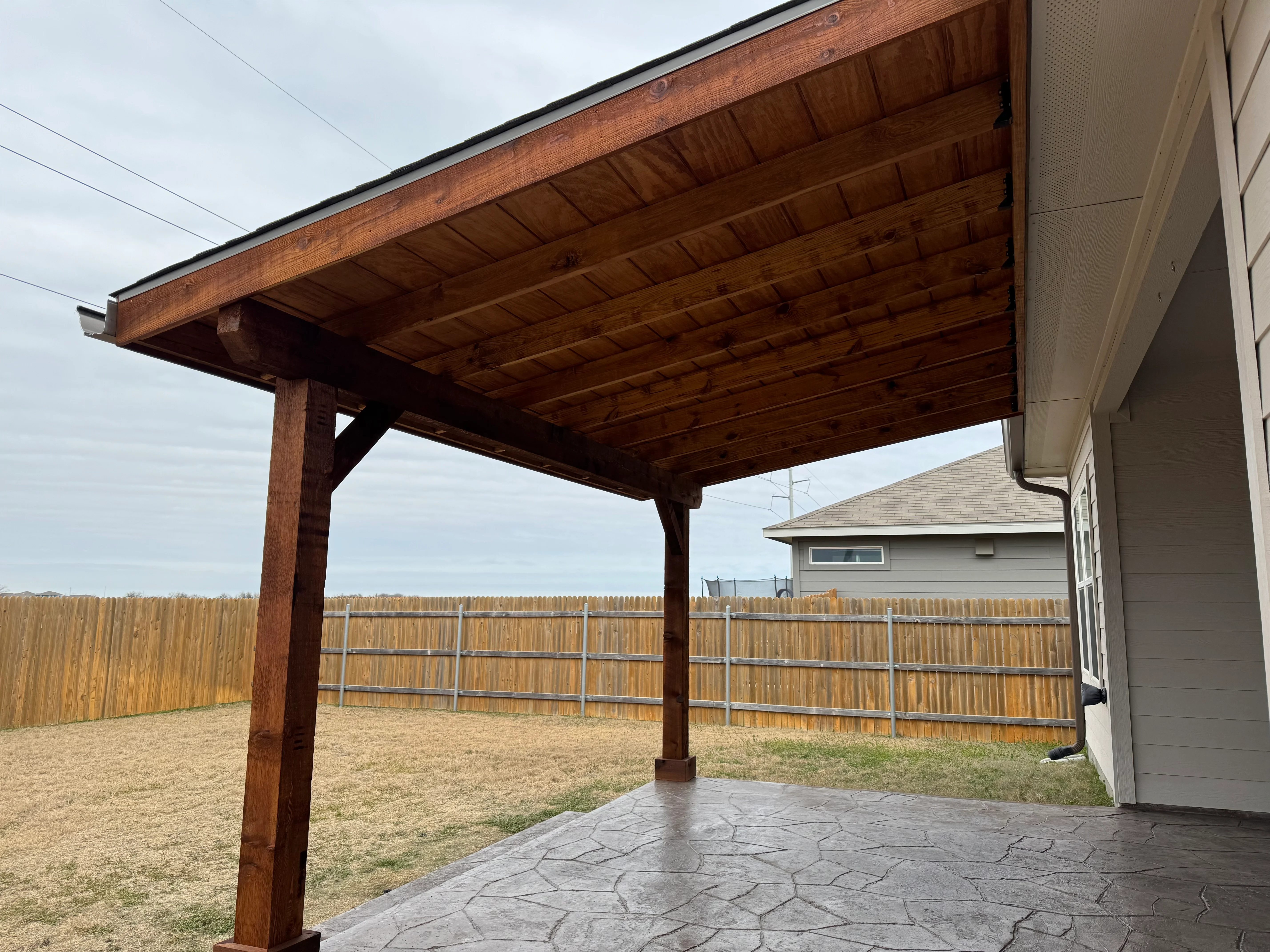 Stained wood patio cover with exposed beam ceiling and stamped concrete floor