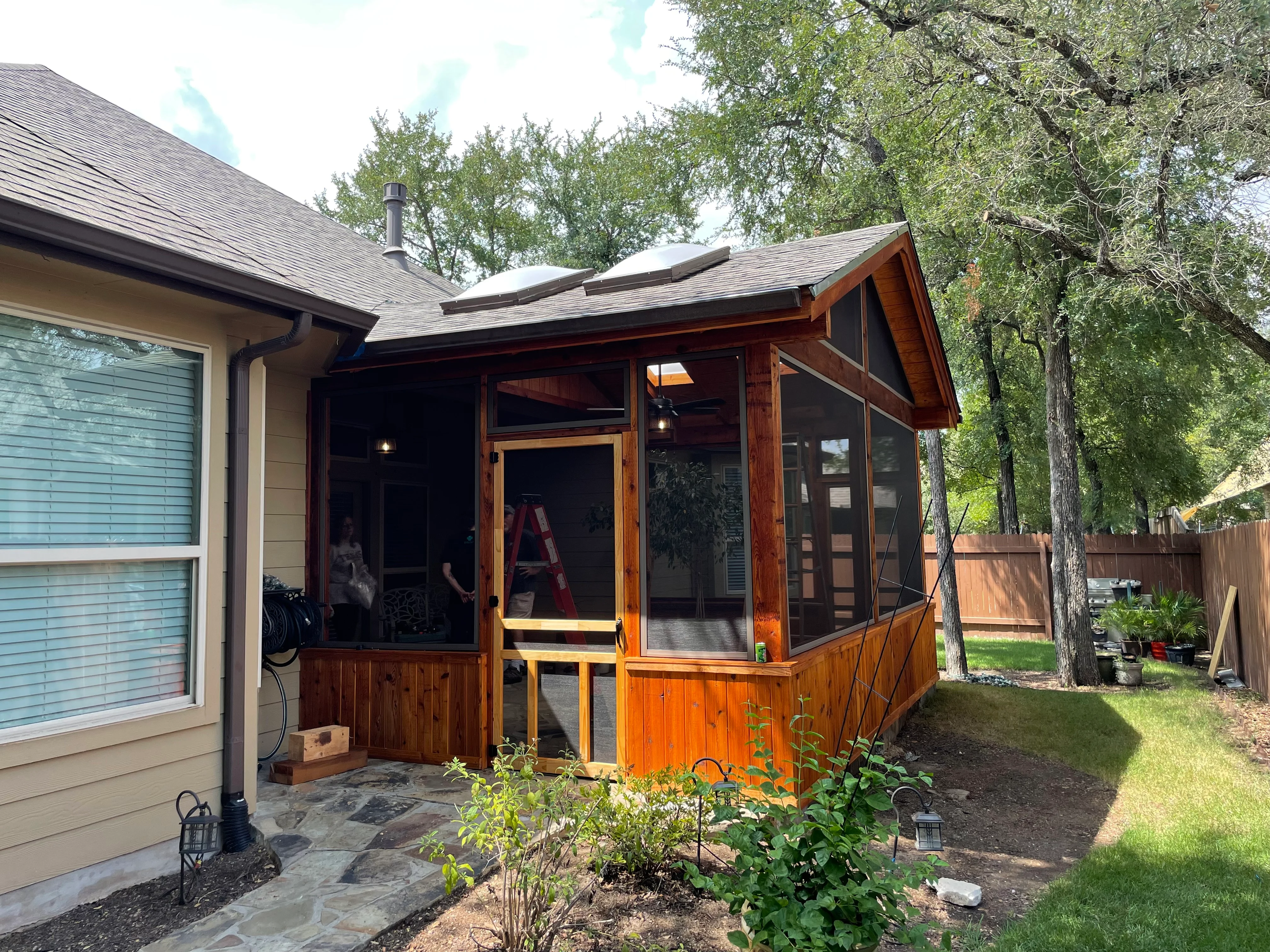 Cedar screened porch with glass panels, wooden railings, and stone patio foundation