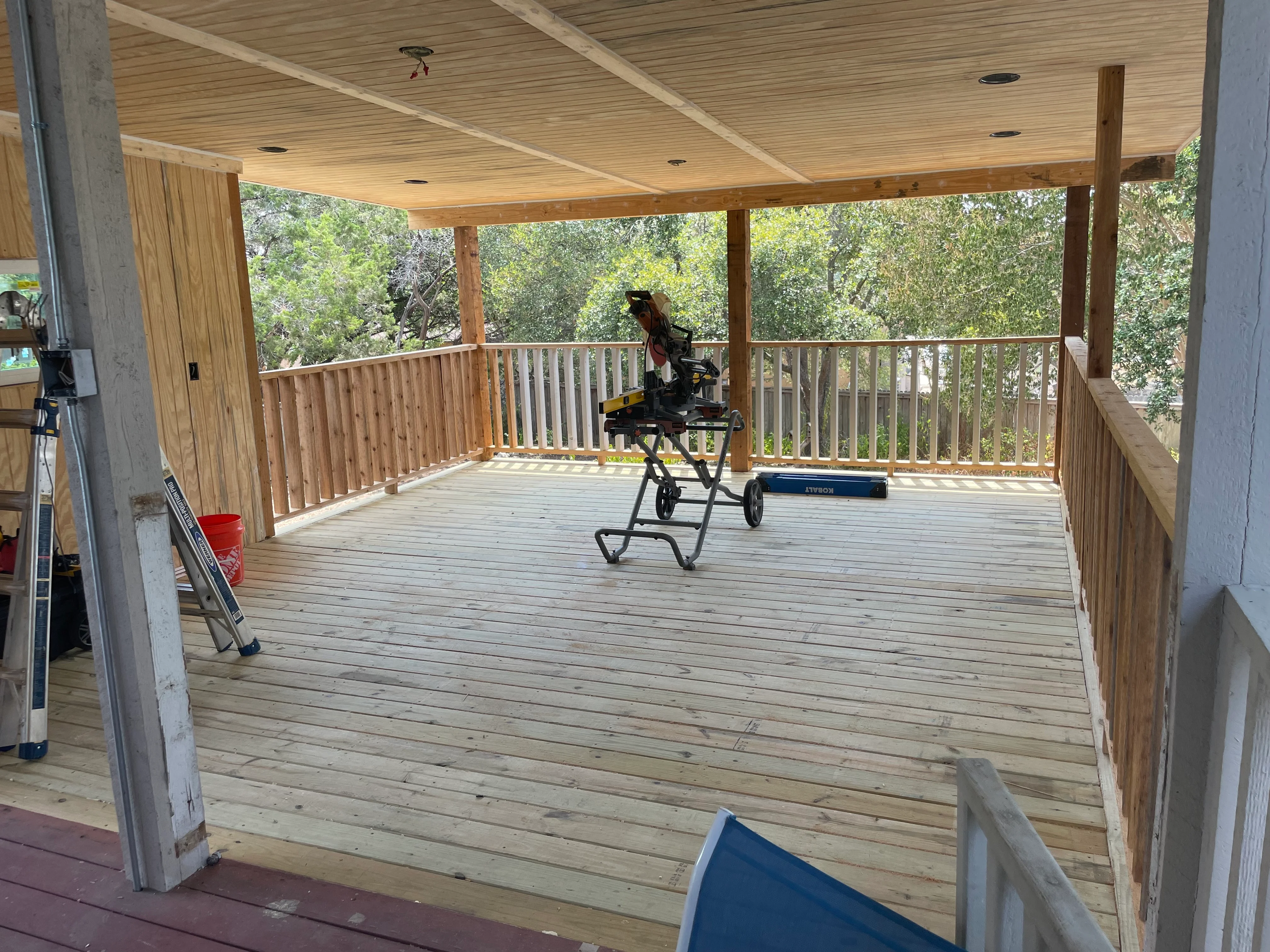 Covered deck with wood decking, vertical railing, and beam ceiling structure overlooking trees