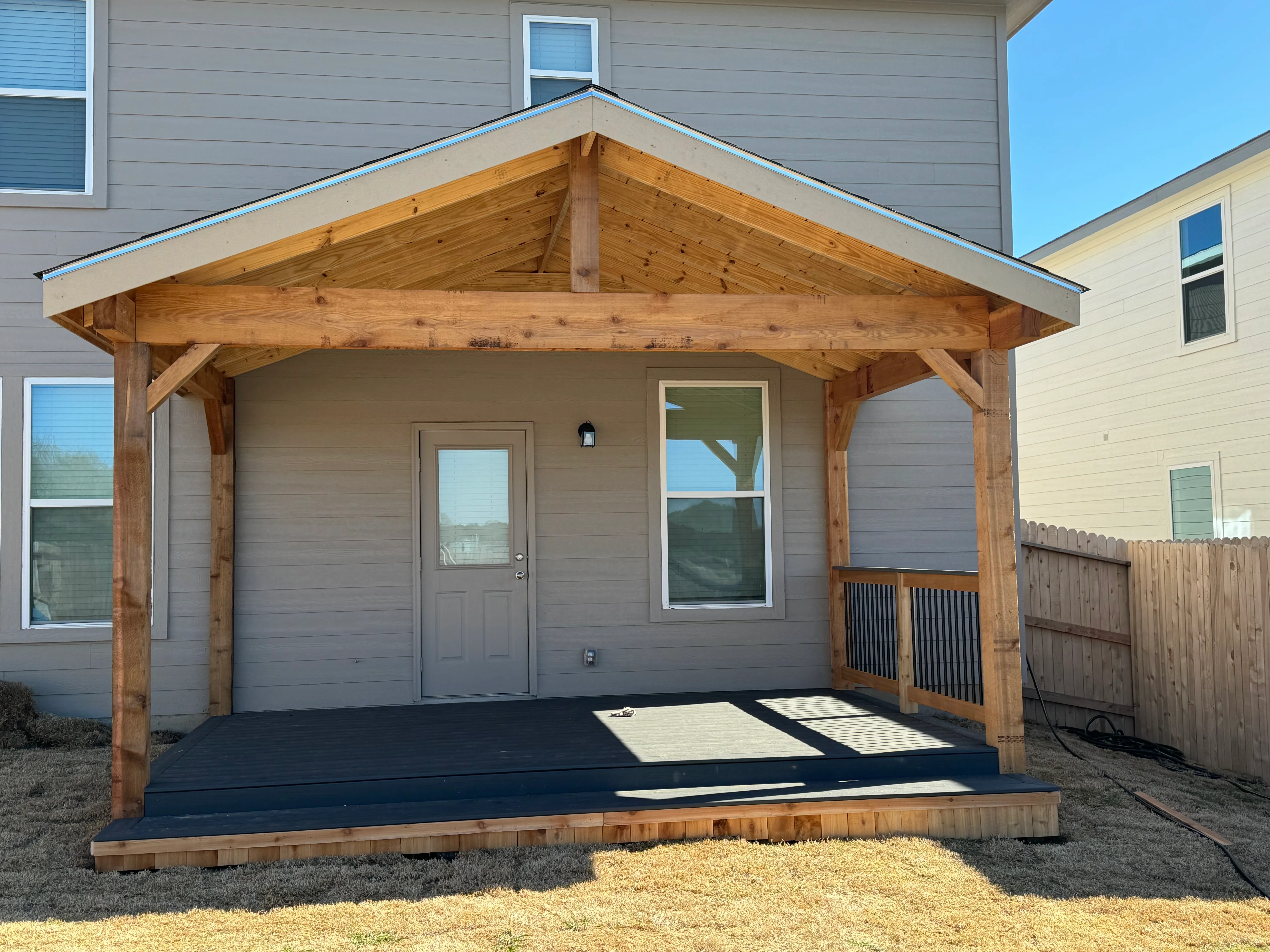 Timber frame patio cover with gable roof and composite deck platform attached to home