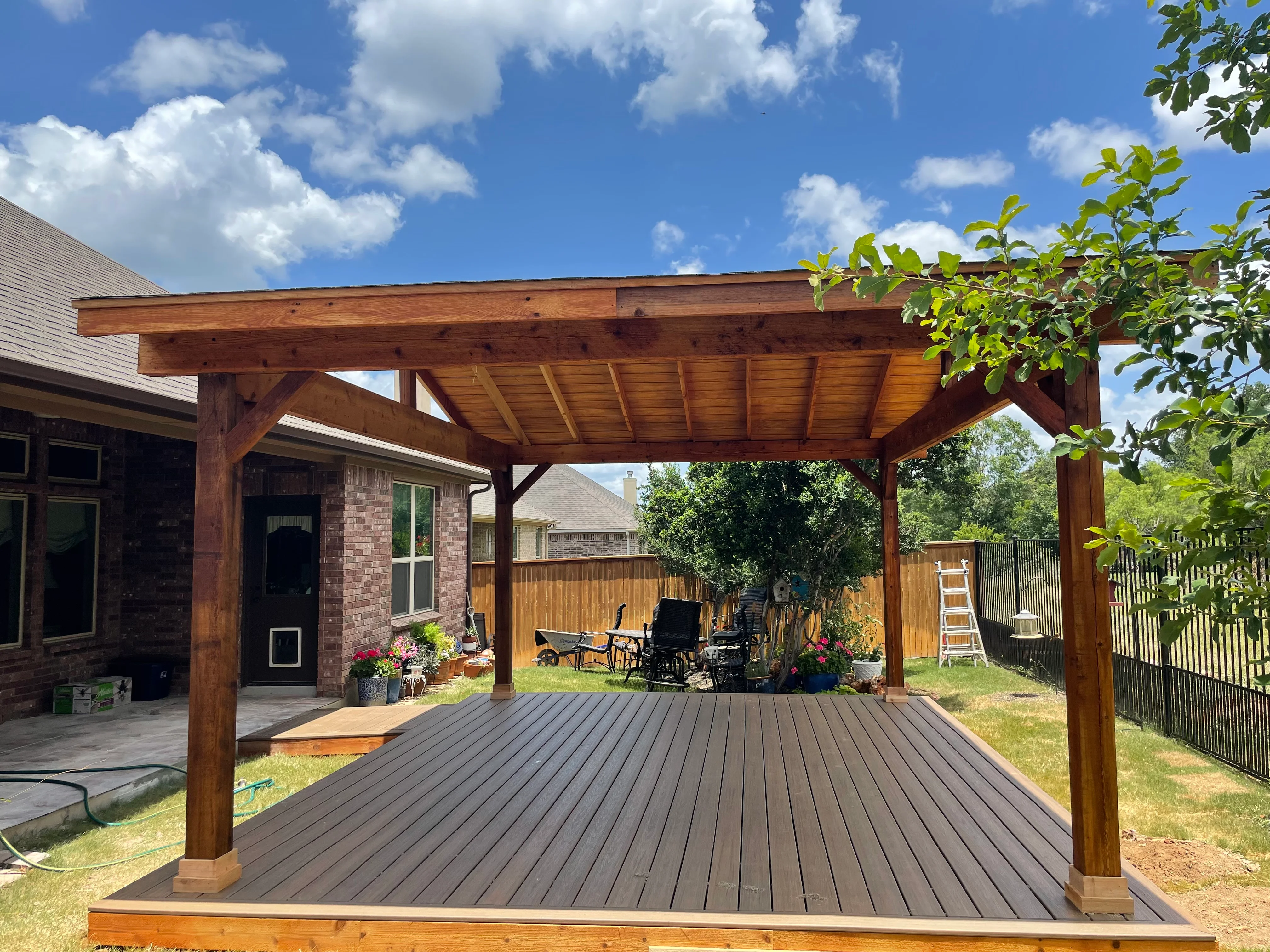 Gray composite deck with wooden pergola, exposed beams and posts, attached to brick home