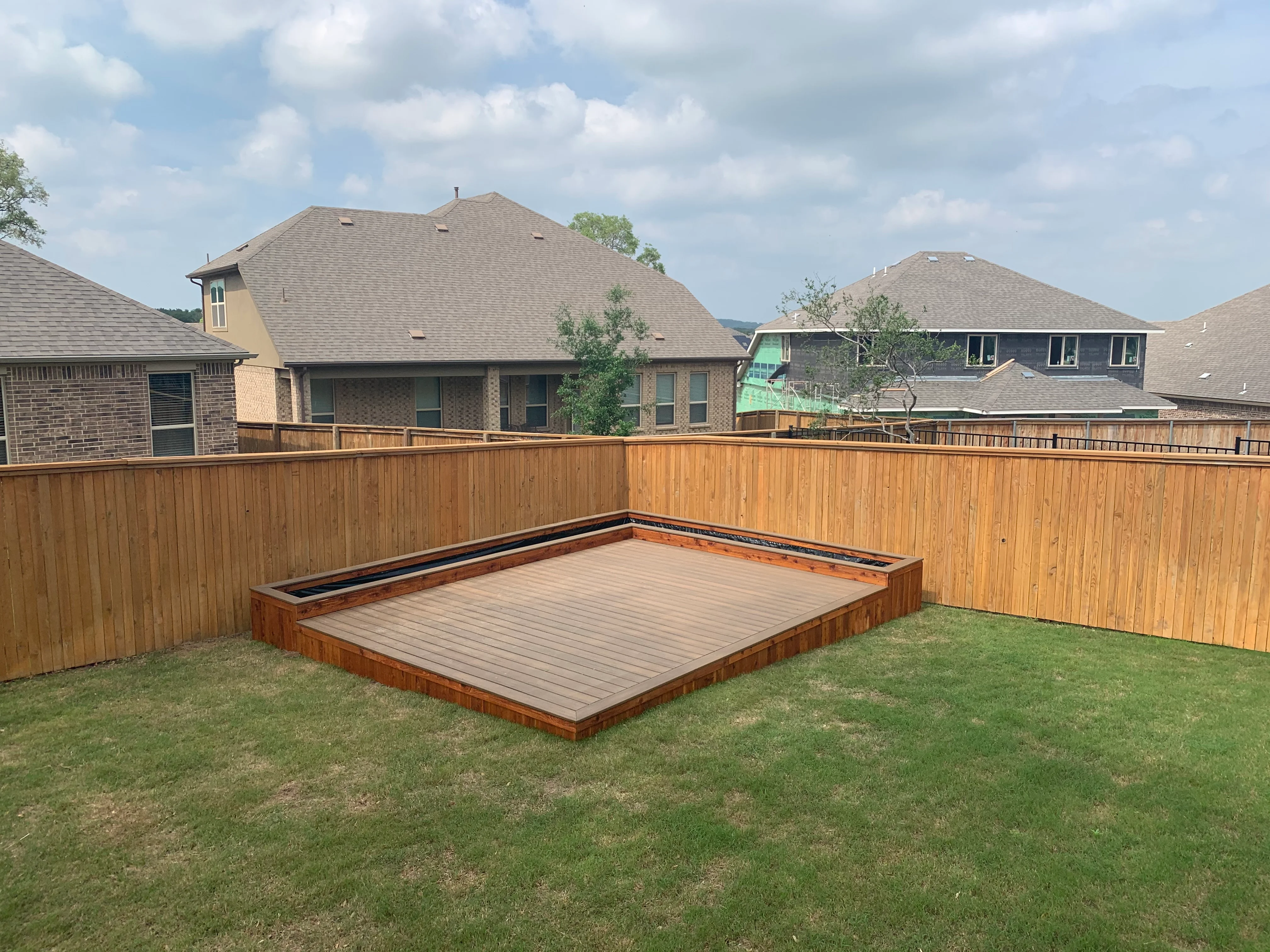 Ground-level composite deck with cedar frame and bench seating in fenced backyard